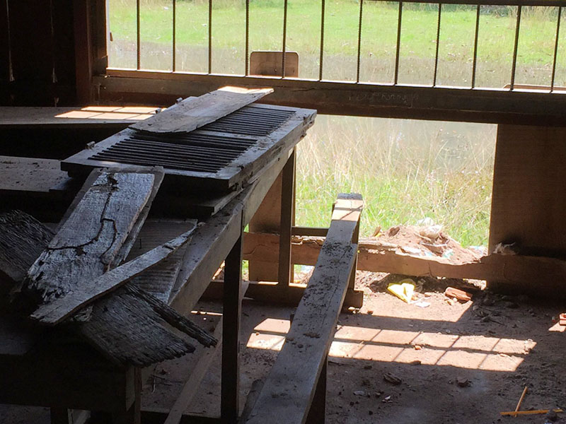 穴が開いた板壁とボロボロの机（机と椅子が一体となって固定されている）